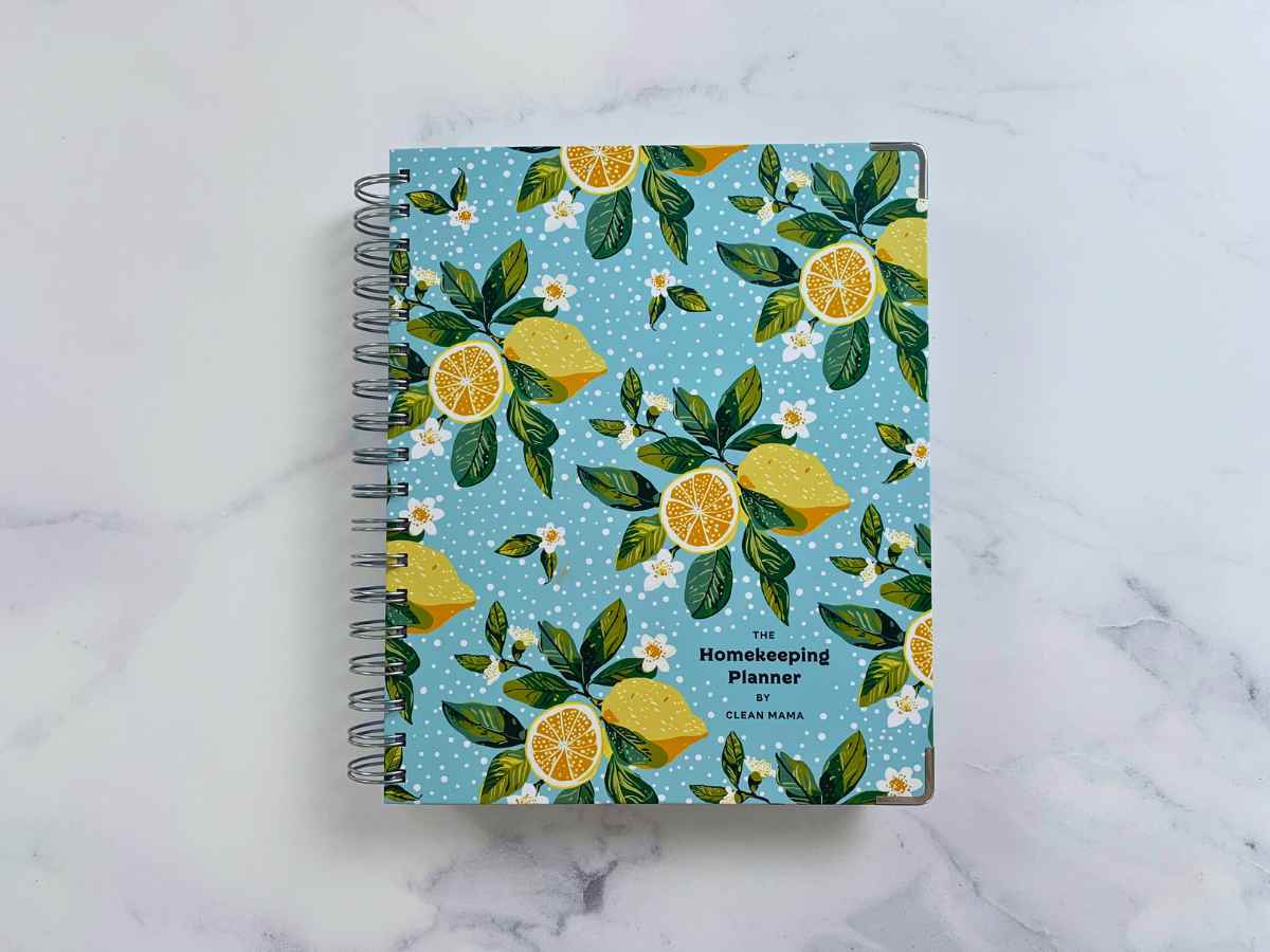 The Clean Mama Planner with blue background and yellow lemons sitting on a white marble counter with grey veining