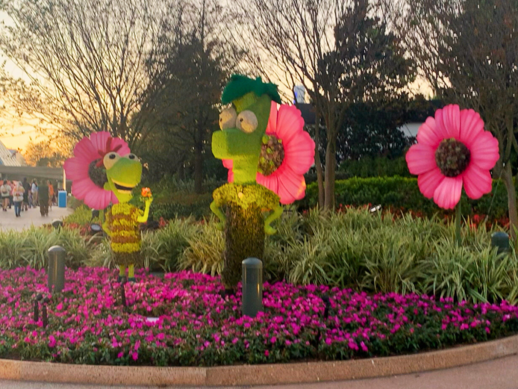 Phineas and Ferb topiaries stand smiling at each other around large pink flowers at EPCOT